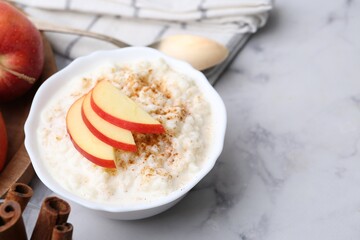 Delicious rice pudding with cinnamon and apples on white marble table, closeup. Space for text