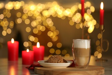 Aromatic coffee in glass, tasty cookies and burning candles on table against blurred Christmas lights. Bokeh effect