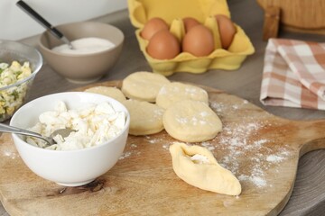 Making pirozhki (stuffed pastry pies). Pieces of dough with cottage cheese on wooden table, closeup