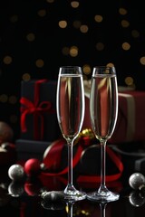 Delicious champagne in glasses and Christmas decor on black mirror surface against blurred lights