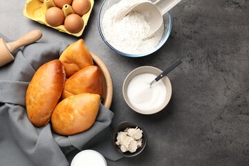 Delicious pirozhki (stuffed pastry pies) and ingredients on grey table, flat lay