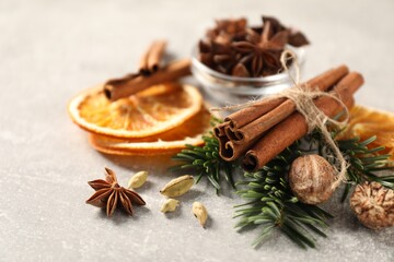 Different spices, dried orange slices and fir tree branches on light grey table, closeup. Christmas season