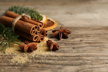 Different spices, dried orange slices and fir tree branches on wooden table, closeup with space for text. Christmas season
