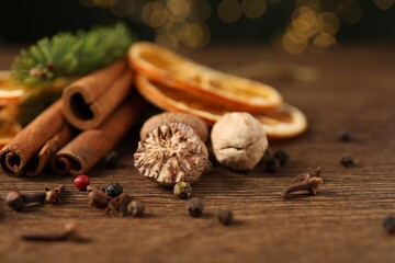 Different spices, dried orange slices and fir tree branches on wooden table, closeup. Christmas season
