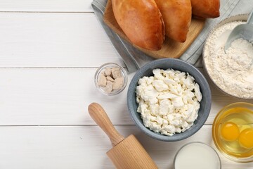 Delicious pirozhki (stuffed pastry pies) and ingredients on white wooden table, flat lay