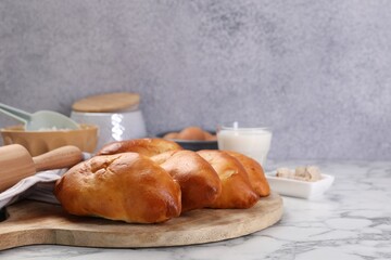 Delicious pirozhki (stuffed pastry pies) and ingredients on white marble table, closeup. Space for text