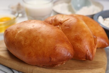Delicious pirozhki (stuffed pastry pies) and ingredients on table, closeup