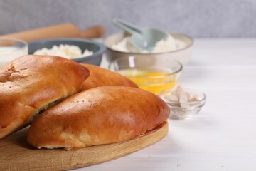 Delicious pirozhki (stuffed pastry pies) and ingredients on white wooden table, closeup