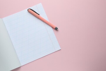 Open copybook and pen on pink background, top view. School stationery