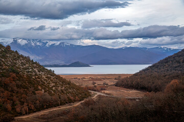 Stunning view of Lake Prespa in Greece, surrounded by snow-capped mountains, forested hills, and serene landscapes under a dramatic cloudy sky