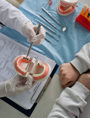 Dentist shows a teenager a jaw of teeth with caries