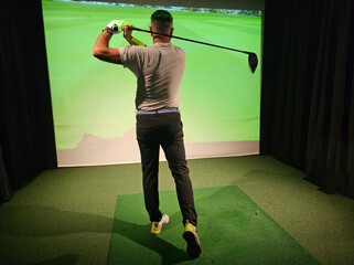Professional male golfer holding club playing golf indoors on golf simulator concept
