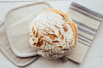 Loaf of homemade sourdough bread in home kitchen on white wood background. 
