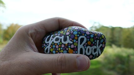 Looking around nature view with hand holding kindness rock