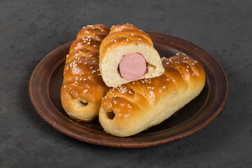 Hot sausage in the dough. On a plate. Dark background