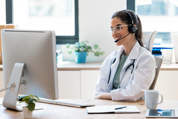 Female doctor explaining medical treatment to patient through a video call with laptop and earphones in the consultation