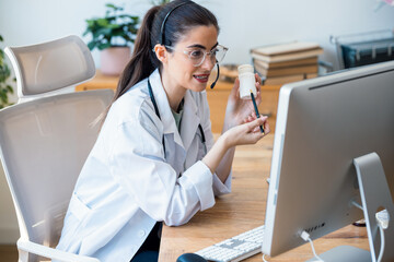 Female doctor explaining medical treatment to patient through a video call with laptop and earphones in the consultation