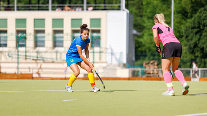Two young female athletes compete in intense field hockey match during sunny day