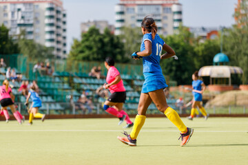 Women playing hockey in colorful uniforms on a sunny day at a local field