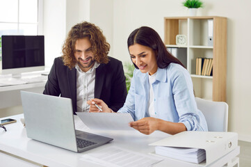 Team of two accountants doing paperwork. Happy young man and woman sitting at an office desk...