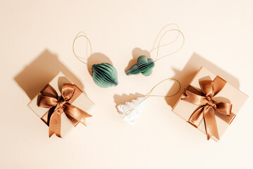 Flat lay of gift boxes with bronze ribbons, green and white paper ornaments on a beige background, top view