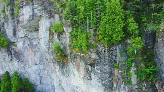 Aerial close-up of an impressive rocky shoreline cliff covered in vegetation and stretching into the sea within the natural landscape of Bic National Park, Quebec., Canada