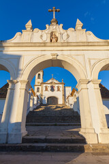Obraz premium A grand church with a whitewashed facade and a prominent bell tower, framed by a stone archway and a staircase leading up to its entrance