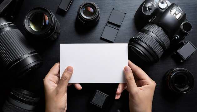 Business card mock up held between hands surrounded by camera gear on a dark surface showcasing a creative workspace