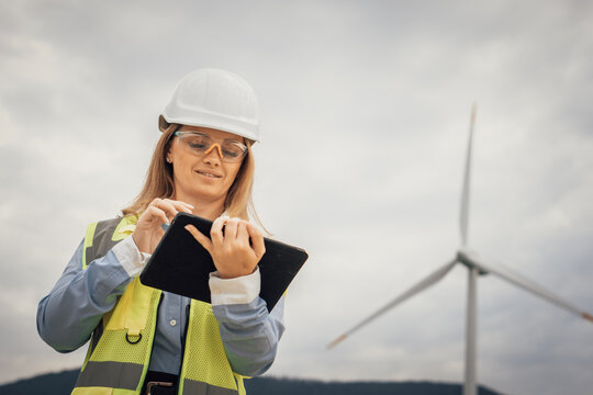 A dedicated female engineer is at a wind farm, using a tablet equipped with advanced technology to conduct thorough data analysis, showcasing innovation and a strong commitment to sustainability