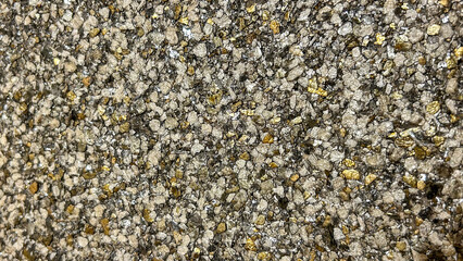Close-up of a textured stone surface with golden and metallic fragments, creating a shimmering effect. Ideal for architectural designs, luxury branding, or creative backgrounds emphasizing opulence.