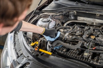 Fototapeta premium Mechanic in gloves servicing a car engine with tools and cloth in a well-lit garage, concept of automotive care and repair