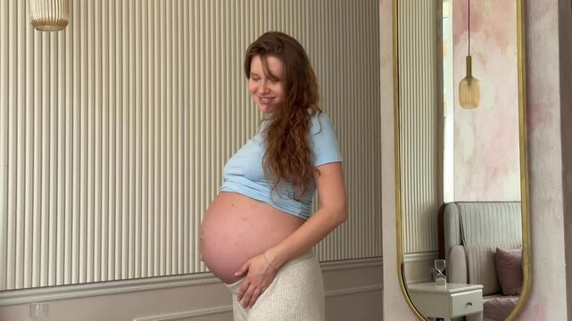 beautiful pregnant woman wakes up and pulls up in the morning in bed in the bedroom and strokes her belly, 3 trimester