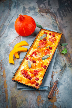 Homemade pampkin savoury tart quiche pastry with prosciutto ham, fresh cheese and cranberries served as close-up in a classical baking form