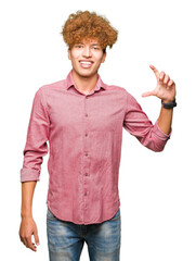 Young handsome business man with afro hair smiling and confident gesturing with hand doing size sign with fingers while looking and the camera. Measure concept.