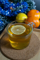 Top-down view of a cup of tea with lemon, surrounded by a Christmas tree, lemon, and mandarins, evoking a festive mood.