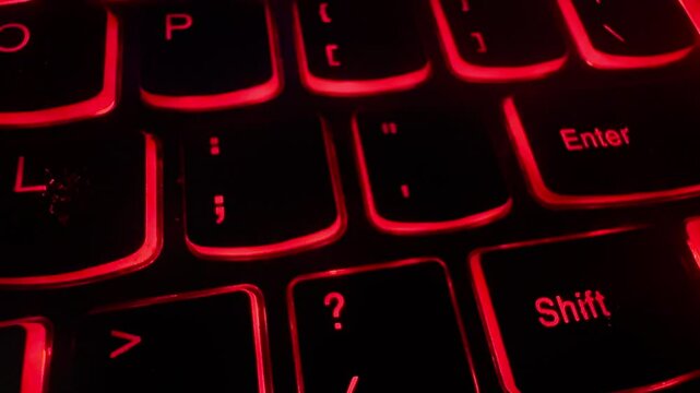 Extreme closeup of an old red backlit laptop computer keyboard. Dolly shot. 80s 90s stylized video with scanlines. Hacking,, thriller, computer technology theme. Cinematic filmic look. 