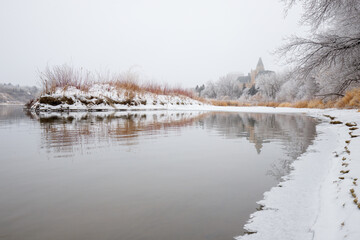 A snowy landscape with a body of water and a large building in the background