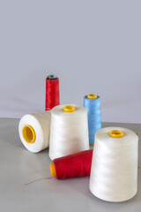 Spools of thread in white, blue, and red colors arranged for use in an embroidery workshop. Representing small business, textile production, apparel branding, and embroidery equipment