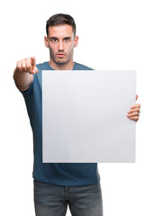 Handsome young man holding advertising banner pointing with finger to the camera and to you, hand sign, positive and confident gesture from the front