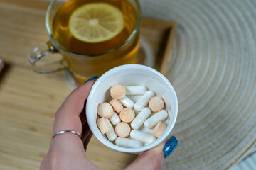 A hand holding a pill organizer with vitamins and supplements. In the background, a green cup of tea creates a cozy, health-focused scene.