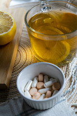 Close-up of vitamins on a white plate, with lemons and a cup of tea in the background, evoking a health and recovery theme.