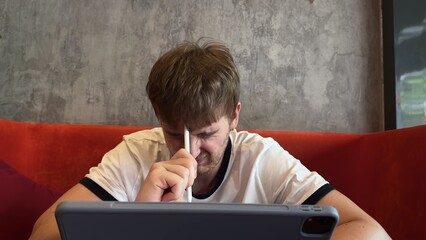 young man upset, irritated, working on a tablet home coffee shop