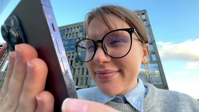 Young woman with myopia wearing eyeglasses with eyesight problems trying to read phone text outdoors