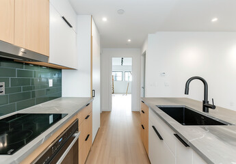Bright modern kitchen with light wood cabinets, green backsplash tiles, and black fixtures, showcasing a sleek and stylish interior design