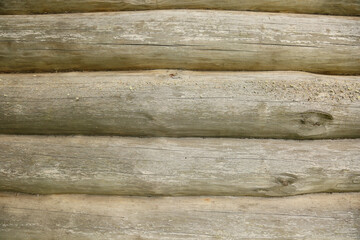 A wall made of logs with the texture of old, weathered light-gray wood