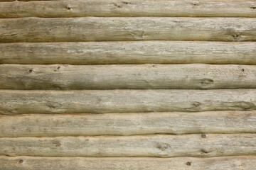 A wall made of logs with the texture of old, weathered light-gray wood