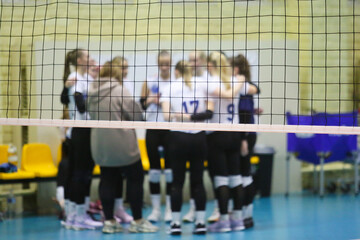 A volleyball net in an indoor court, with volleyball players blurred in the background