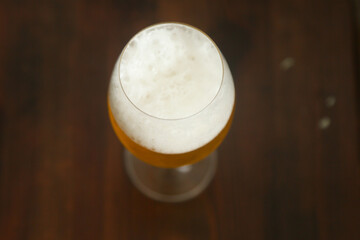 A full glass of beer with a frothy head on top, standing on a table
