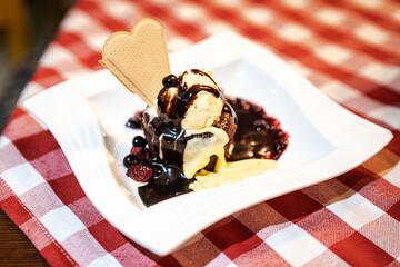 A delightful dessert featuring vanilla ice cream topped with warm berry sauce and a heart-shaped cookie served on a checkered tablecloth.