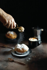 Food photography - a pastry sprinkled with powdered sugar using a sieve from above, capturing the fine particles of sugar falling onto the pastry's surface - photographed on a wooden table, dark mood